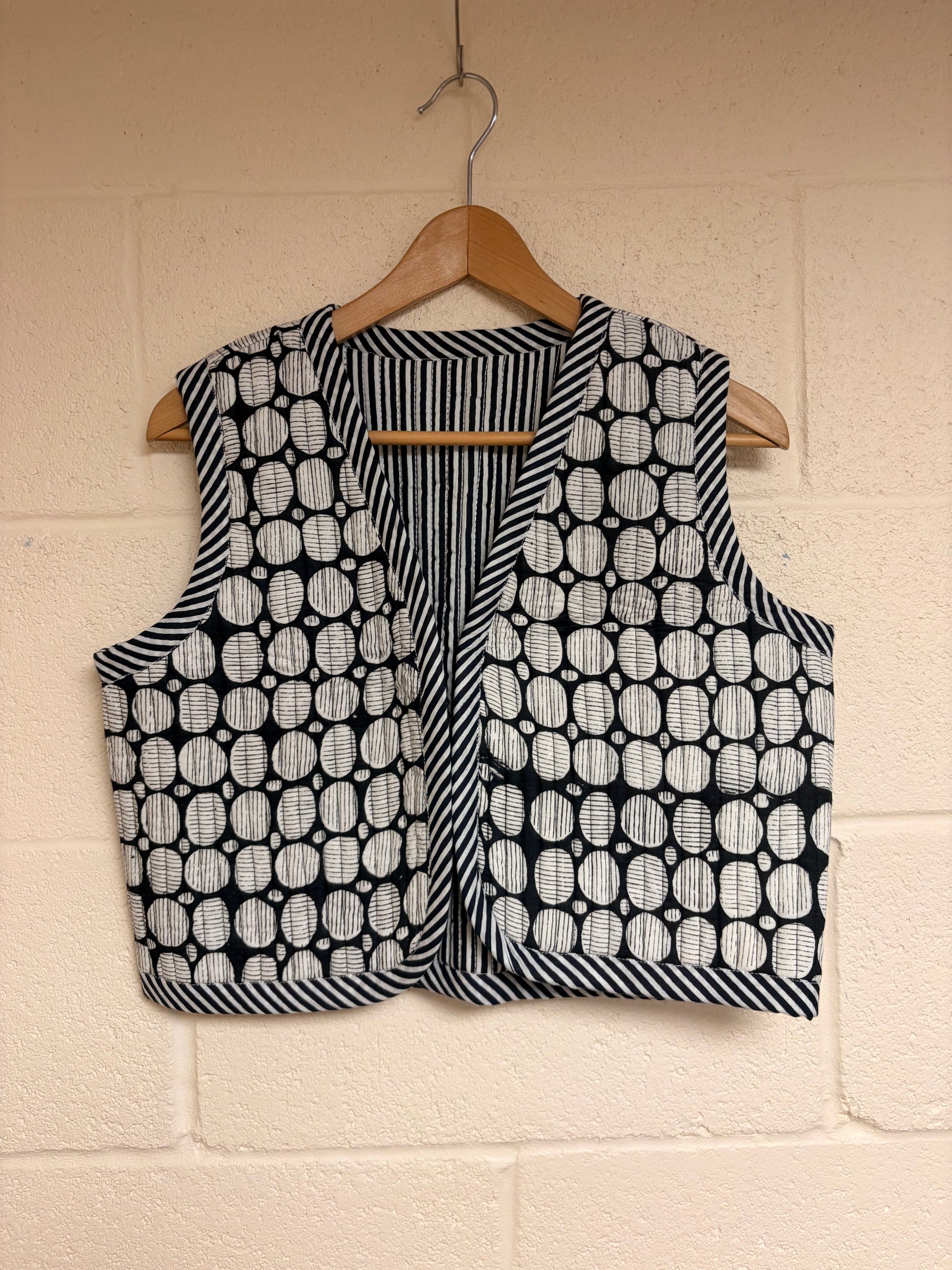 Black and white patterned vest on a hanger against a beige wall.
