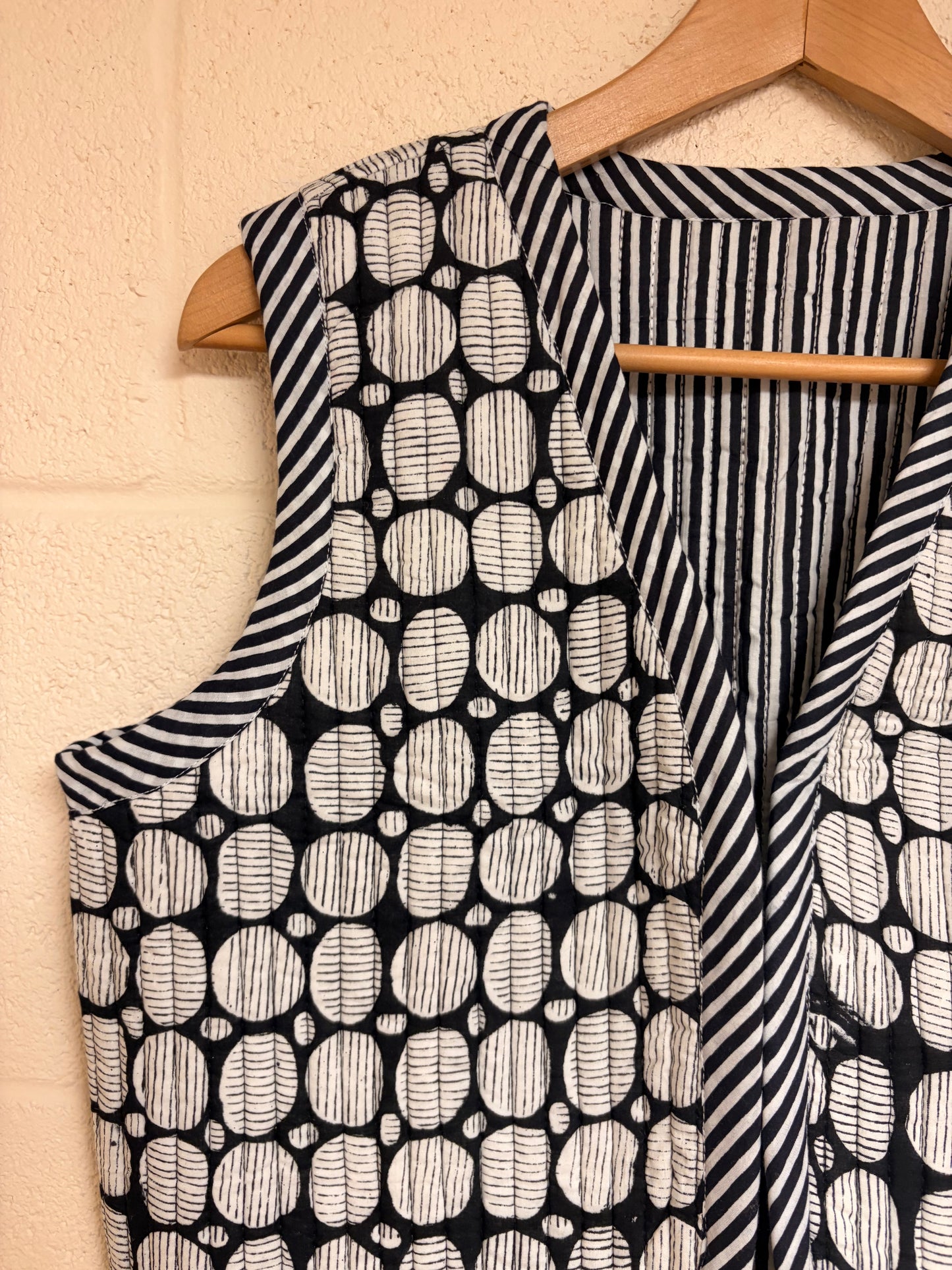 Black and white patterned garment on a wooden hanger against a beige wall.