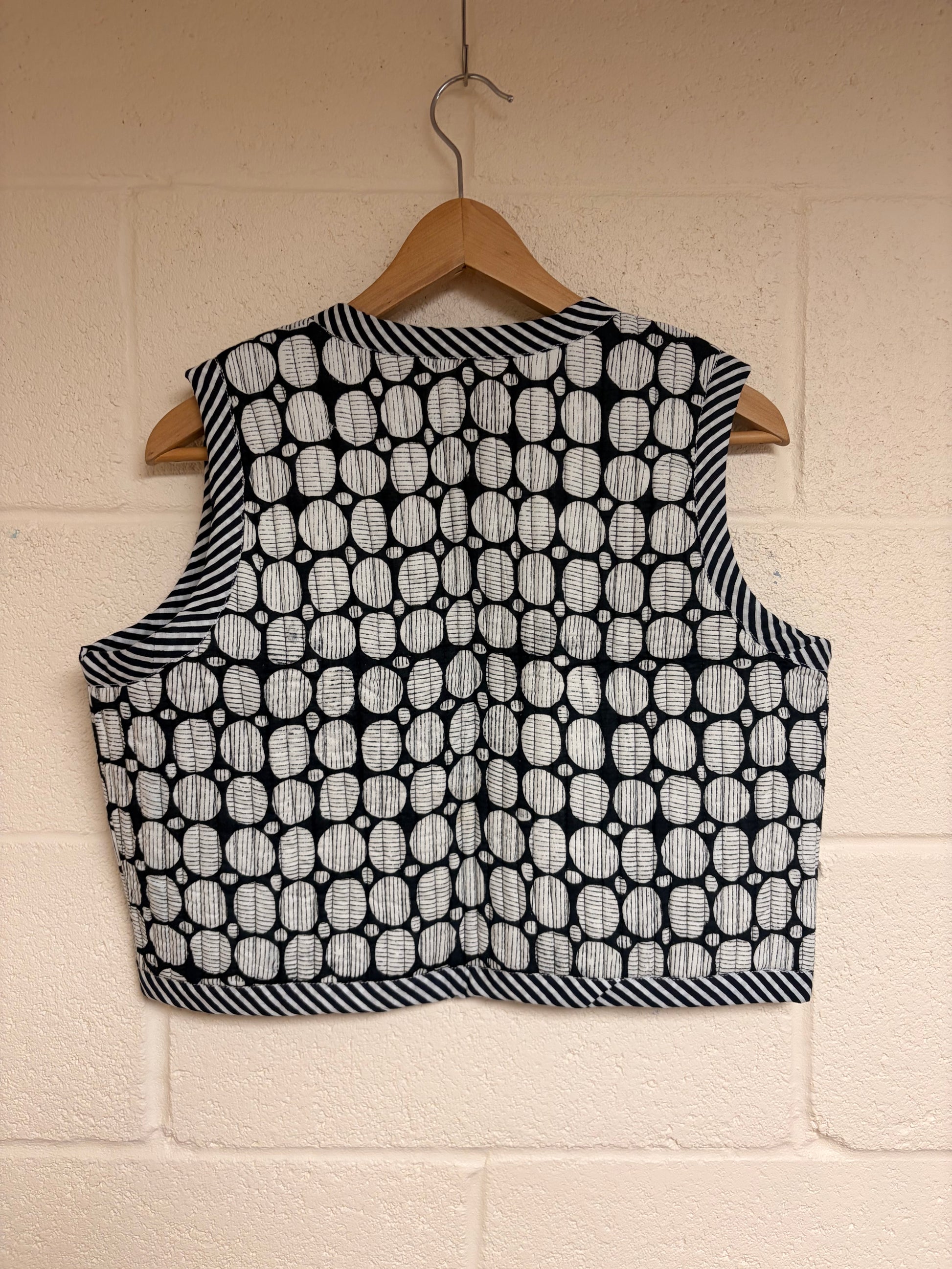 Black and white patterned vest on a wooden hanger against a beige wall.