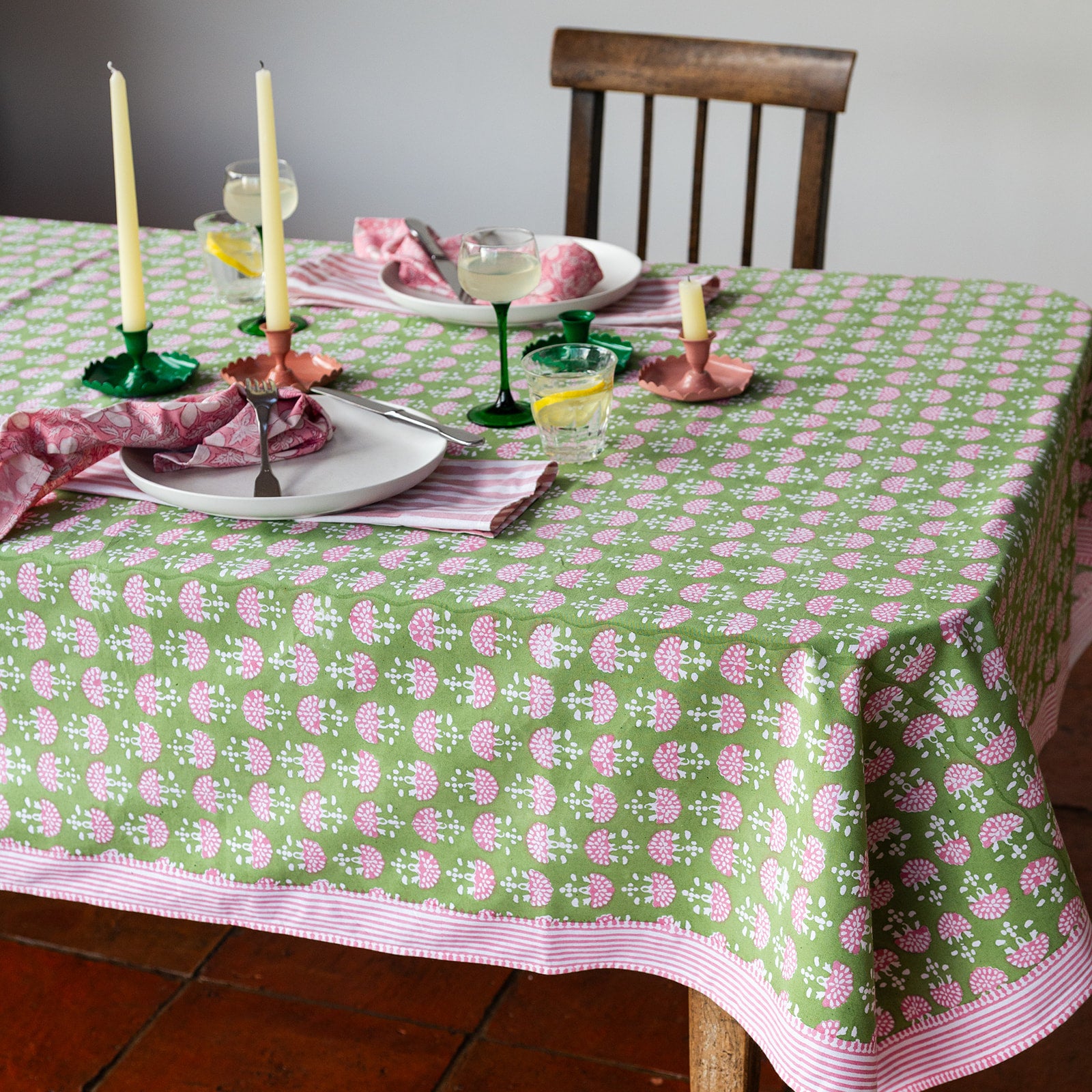 Table setting with a green and pink patterned tablecloth, candles, and glasses.