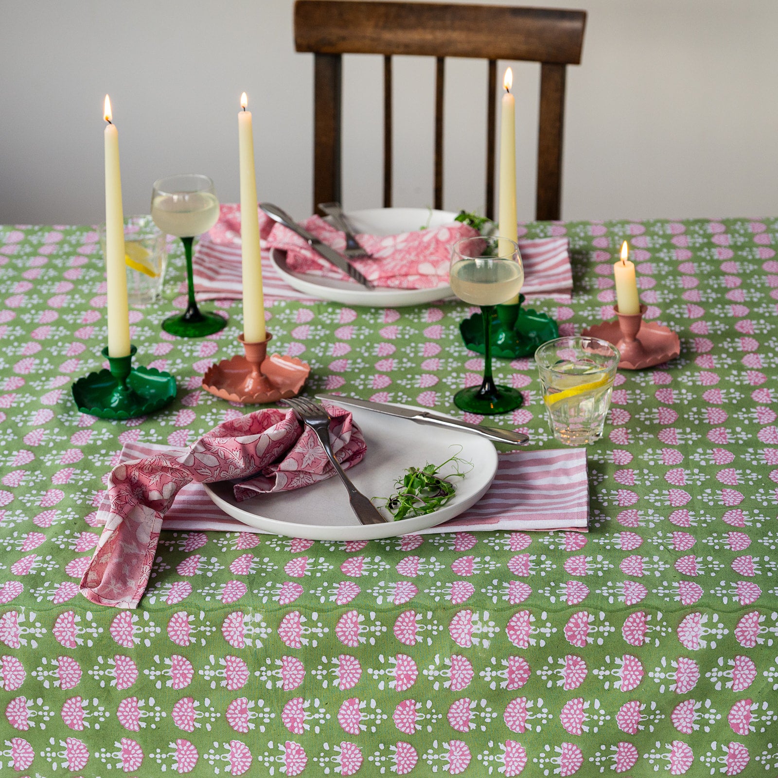 Dining table set with a floral tablecloth, candles, and cutlery.