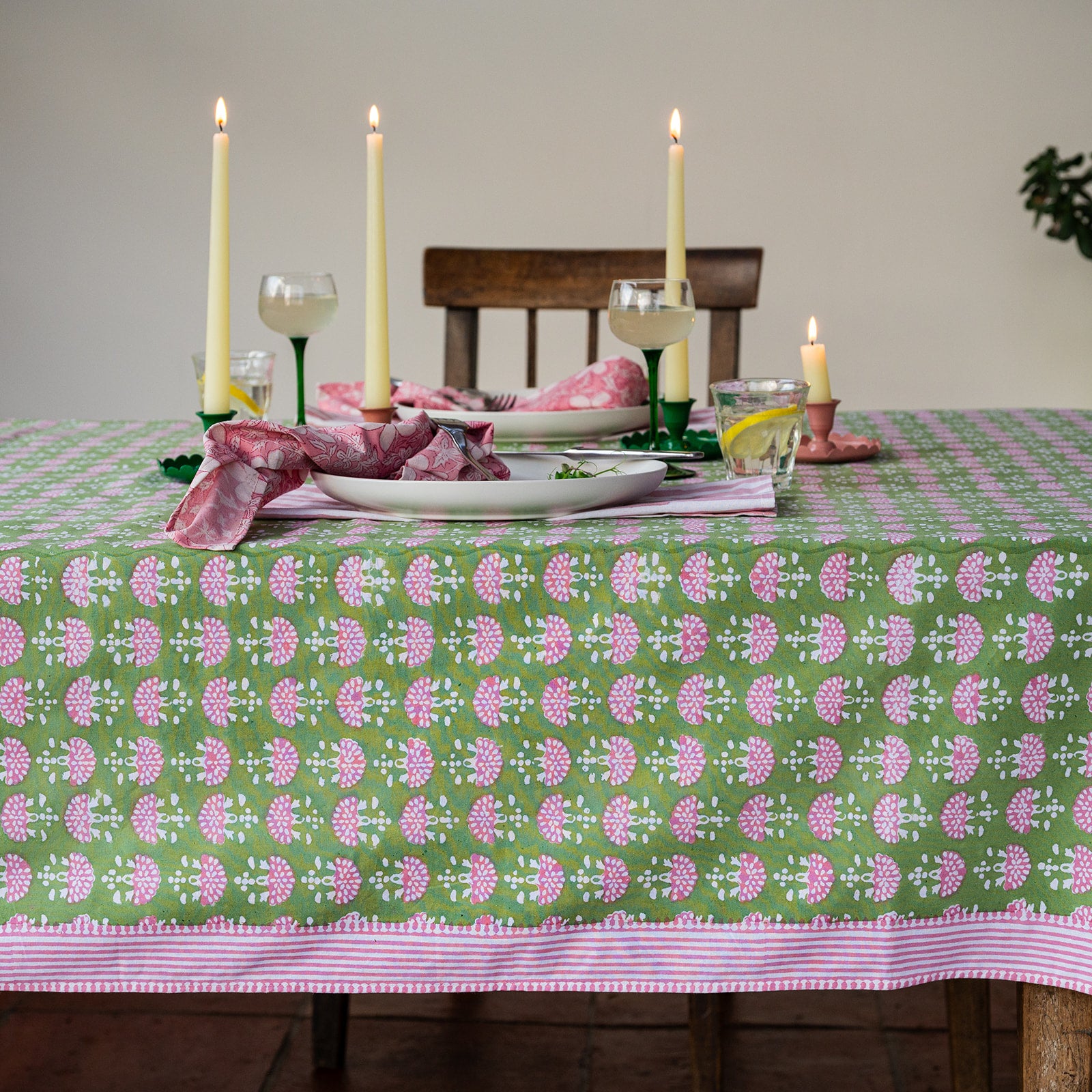 Dining table set with a green and pink patterned tablecloth, candles, and glasses.