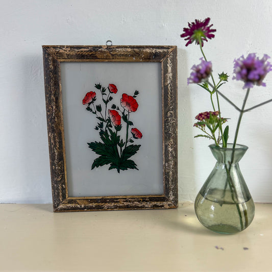 Framed artwork of red flowers next to a vase with purple flowers on a light surface. indian-glass-painting-painting-red-flower
