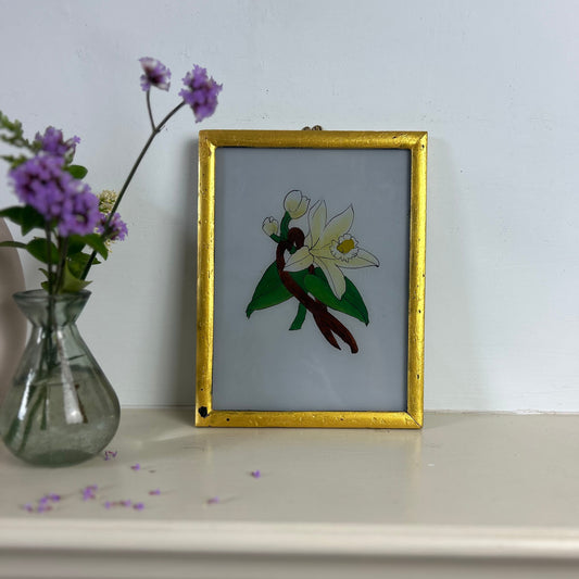 Framed artwork of a bird with flowers on a shelf next to a vase with purple flowers. indian-glass-painting-reverse-art-flower