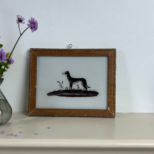 Framed silhouette of a dog on a white surface with a vase of purple flowers.indian-glass-painting-reverse-whippet