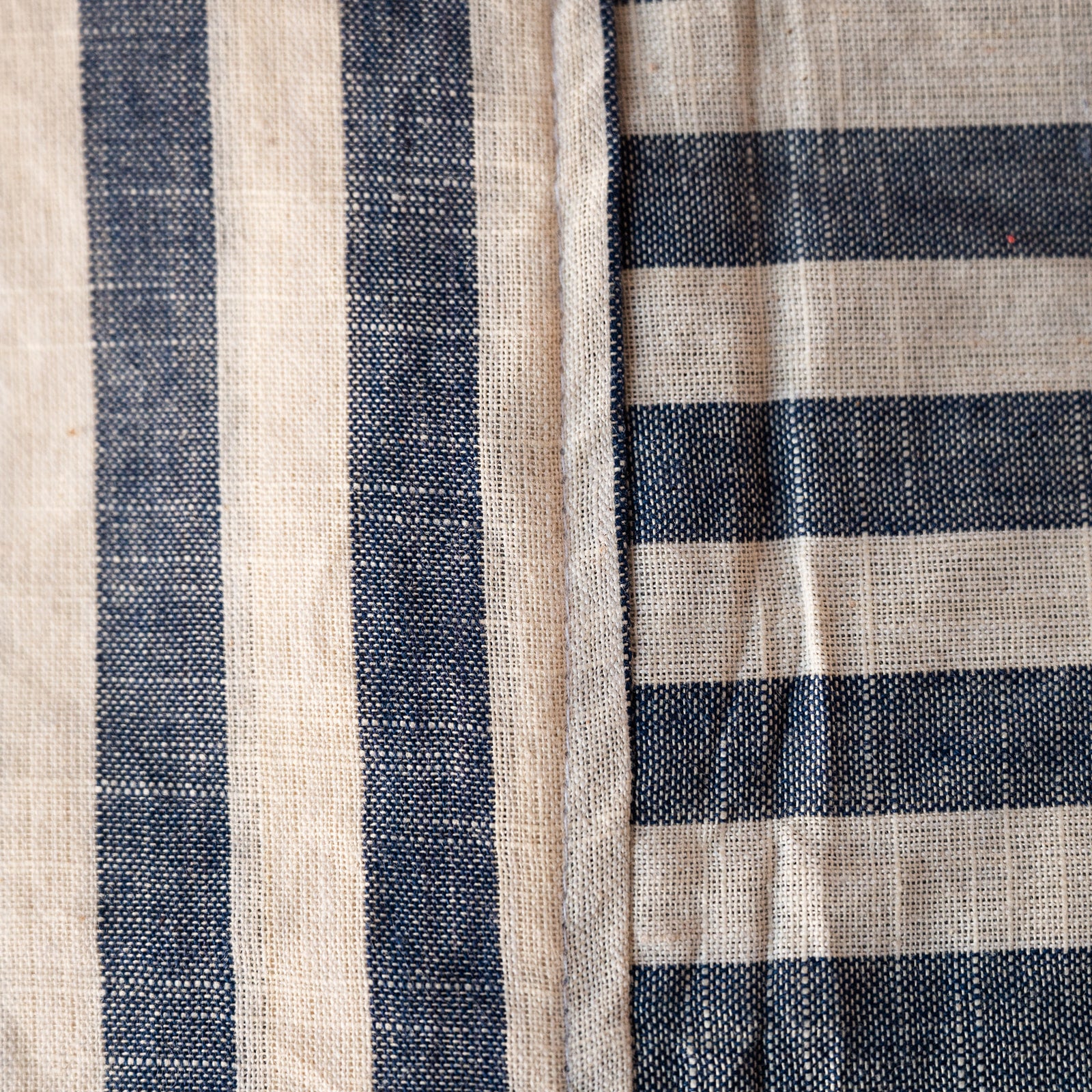 A close-up of a woven textile with alternating vertical navy blue and warm beige stripes, showing the fabric texture and seam details.
