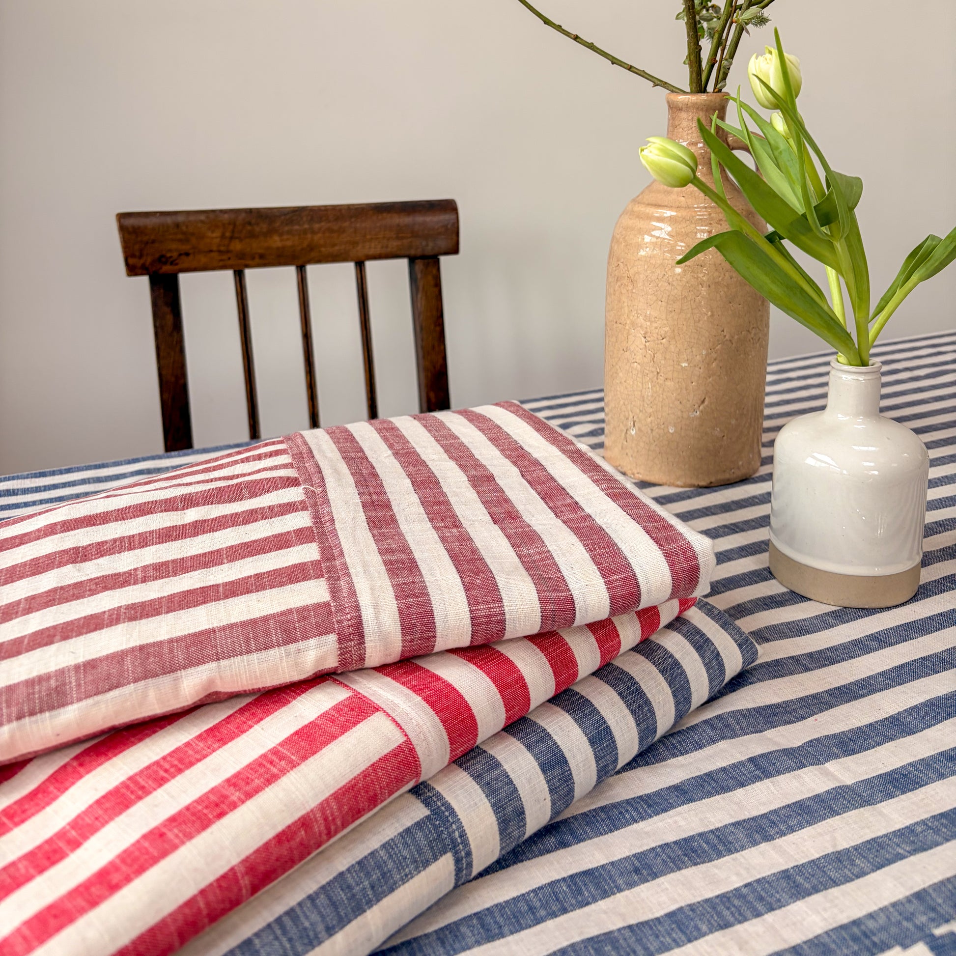 Stack of red, white, and blue striped fabric on a table with a vase and flowers in the background.