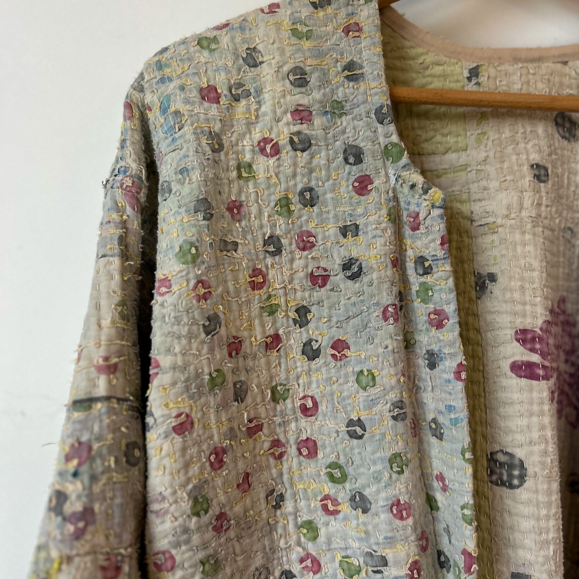 Textile with floral pattern on a wooden hanger against a white background. intage-kantha-jacket-handmade-unique-42-textured-collar