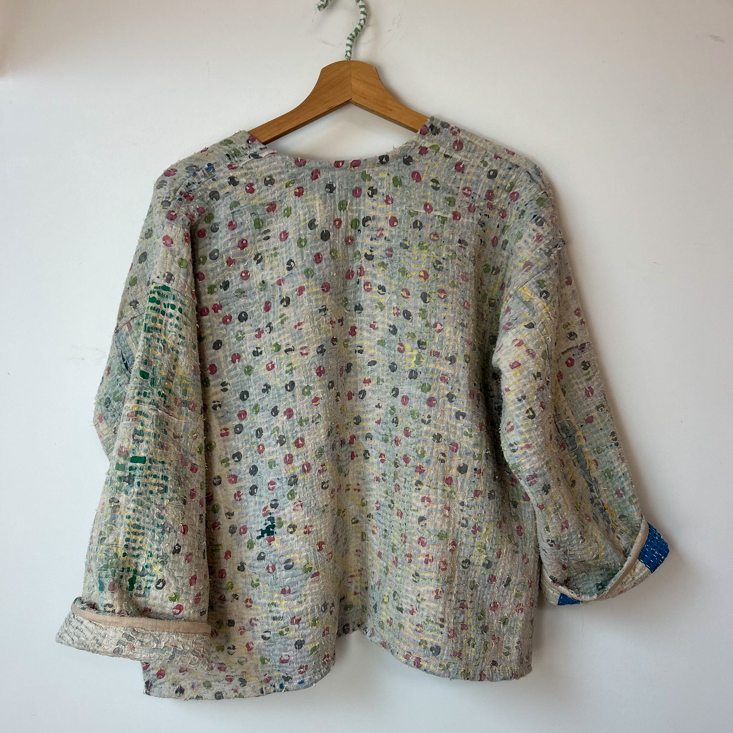 Floral patterned shirt on a wooden hanger against a white wall. intage-kantha-jacket-handmade-unique-42-textured-reverse