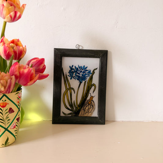 Framed artwork of flowers on a white surface with tulips in the background