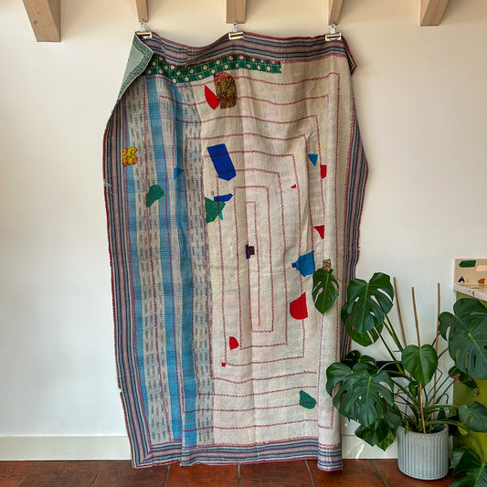 Colorful patterned skirt hanging on a rack against a white wall with a plant in the foreground. kantha-vintage-2027 - hand-made-blanket-throw-textiles-wall-hanging