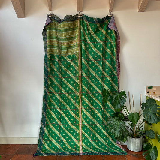 Green patterned fabric draped over a wooden frame against a white wall with a plant in the corner.
