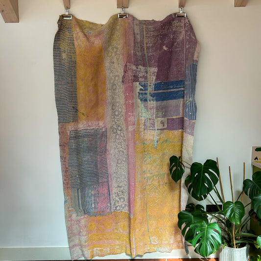 Colorful patchwork dress hanging on a rack with a plant in the background. kantha-vintage-2032 - hand-made-blanket-throw-textiles-wall-hanging