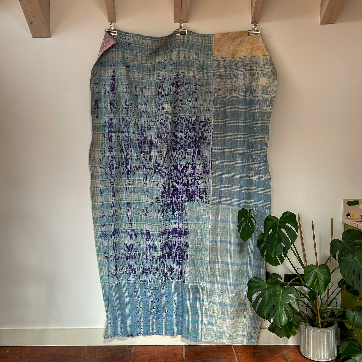 Patchwork skirt with blue and green patterns hanging on a rack against a white wall. kantha-vintage-2032 - hand-made-blanket-throw-textiles-wall-hanging