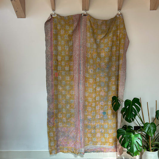 Yellow floral patterned fabric hanging on a wooden rod with a plant in the background.
