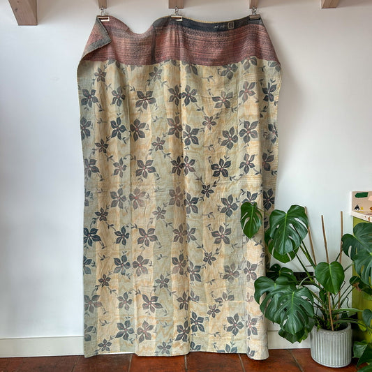 Floral patterned curtain hanging against a white wall with a plant in the foreground.