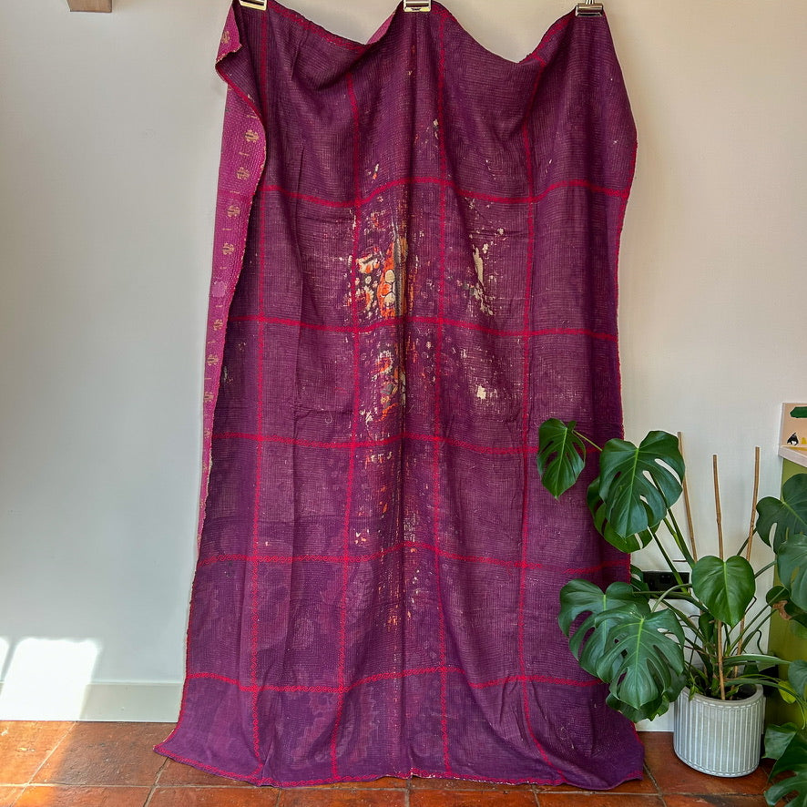 Purple checkered curtain with floral patterns draped over a mannequin against a white wall.