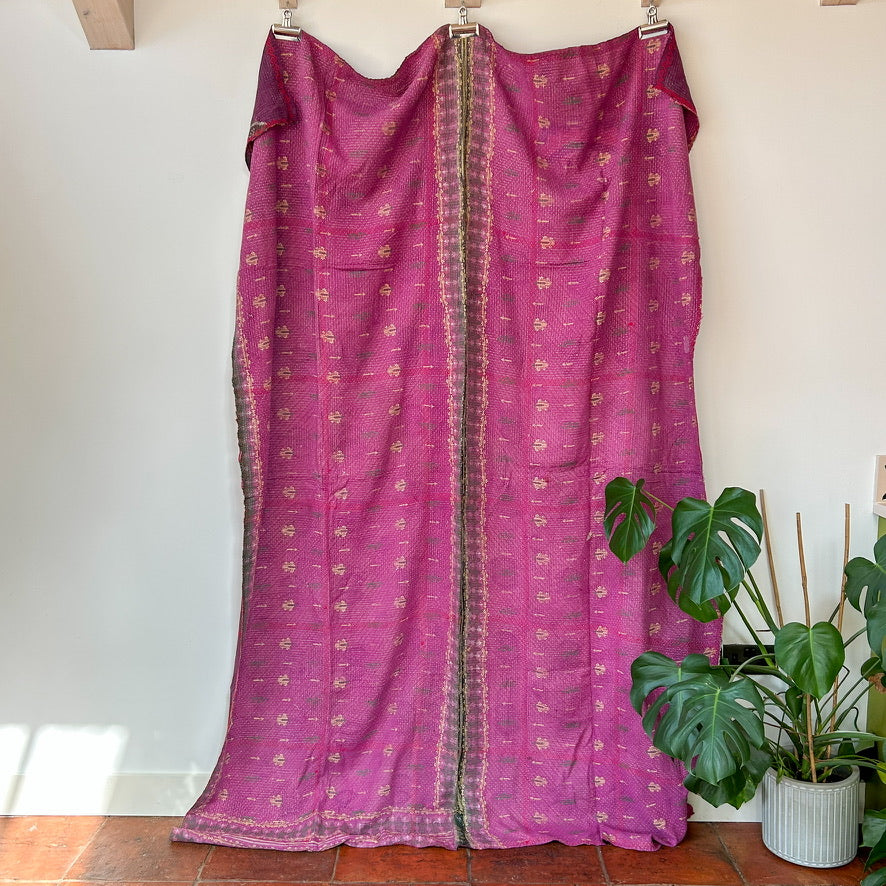 Purple fabric with gold patterns draped over a wooden frame against a white wall.