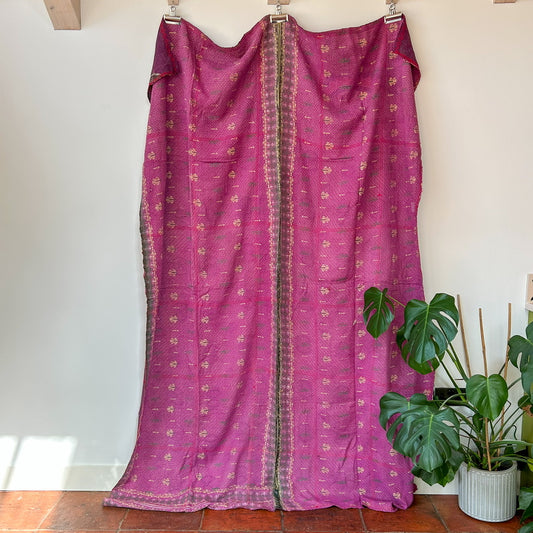 Purple fabric with gold patterns draped over a wooden frame against a white wall.