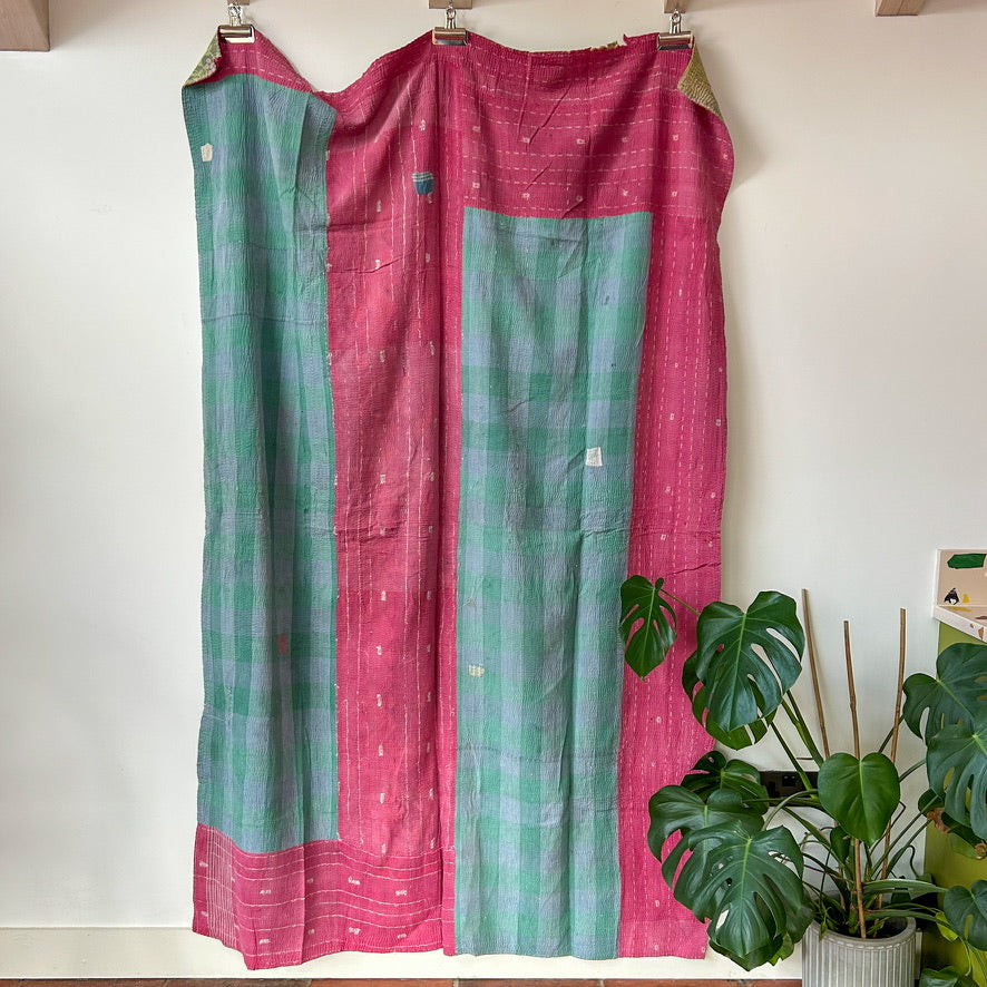 Pink and green checkered curtain with a plant in the background