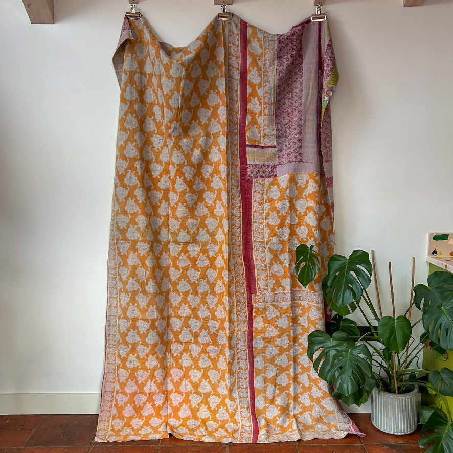 Patterned dress with orange and white design on a wooden floor with a plant in the background