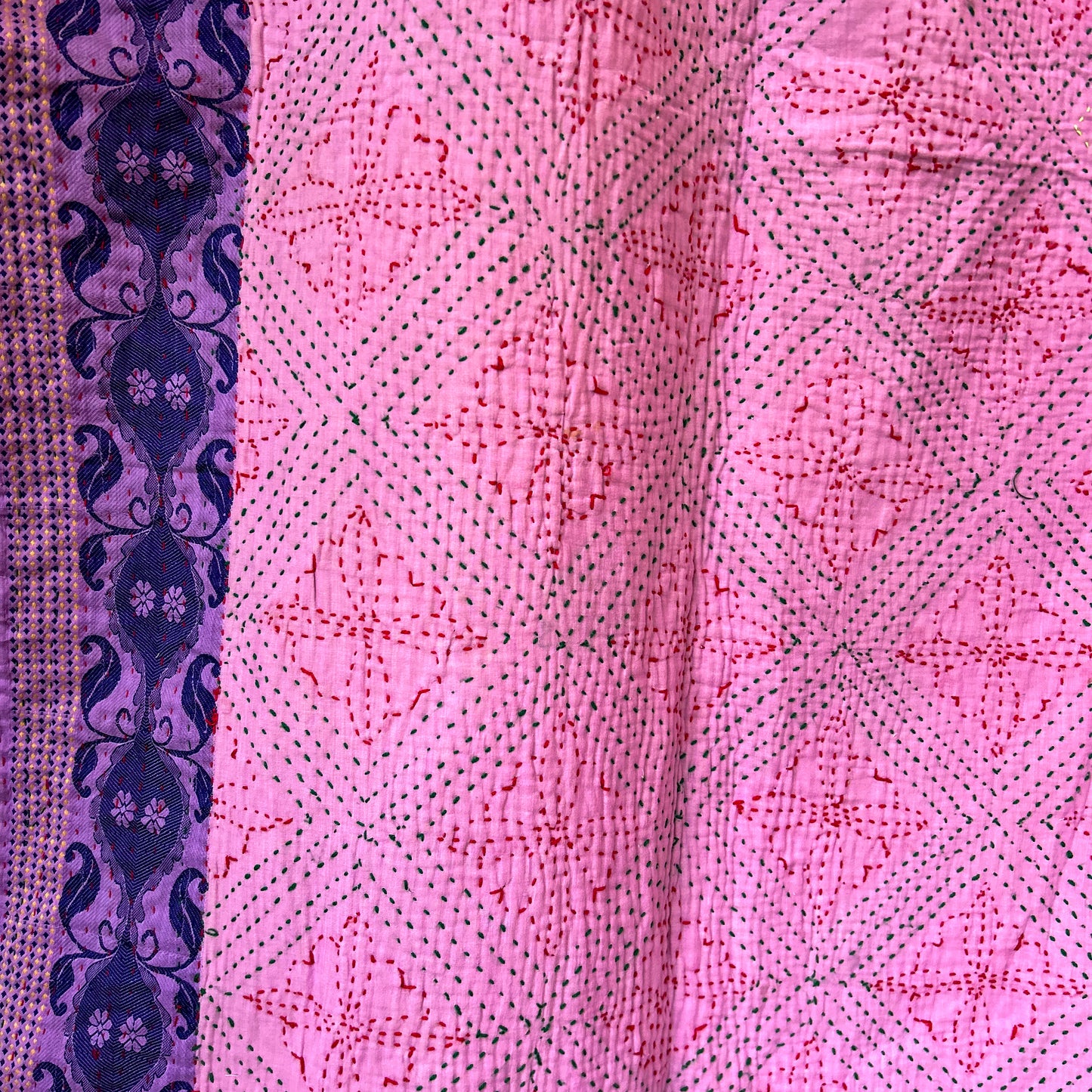 Close-up of pink kantha with intricate patterns and a purple border. stitching