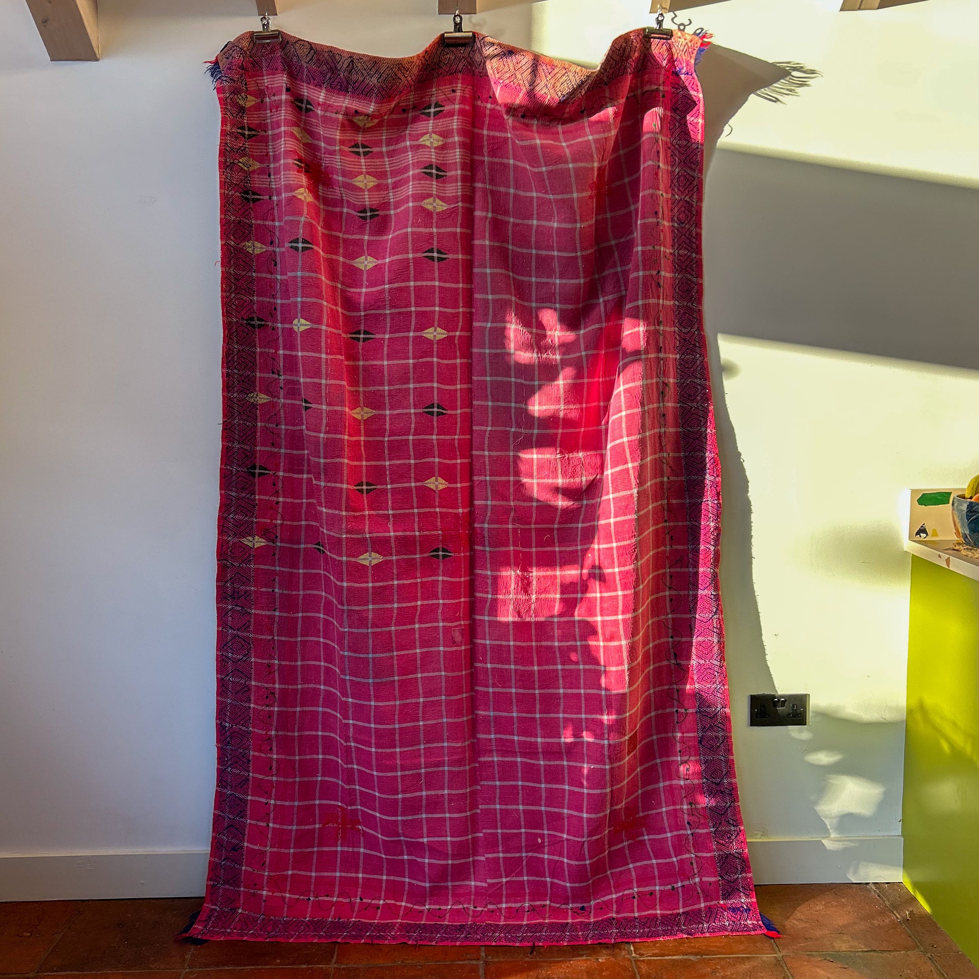 Red plaid dress hanging on a rack against a white wall.