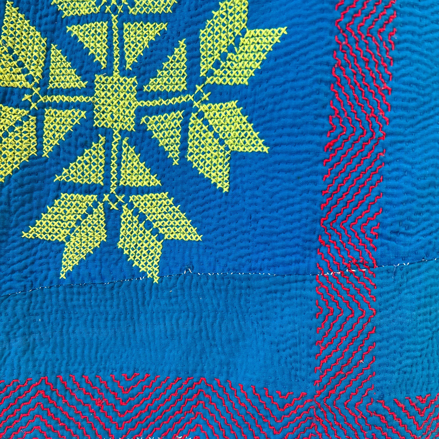 Close-up of a fabric with green leaf pattern on blue background and red zigzag pattern on side.
