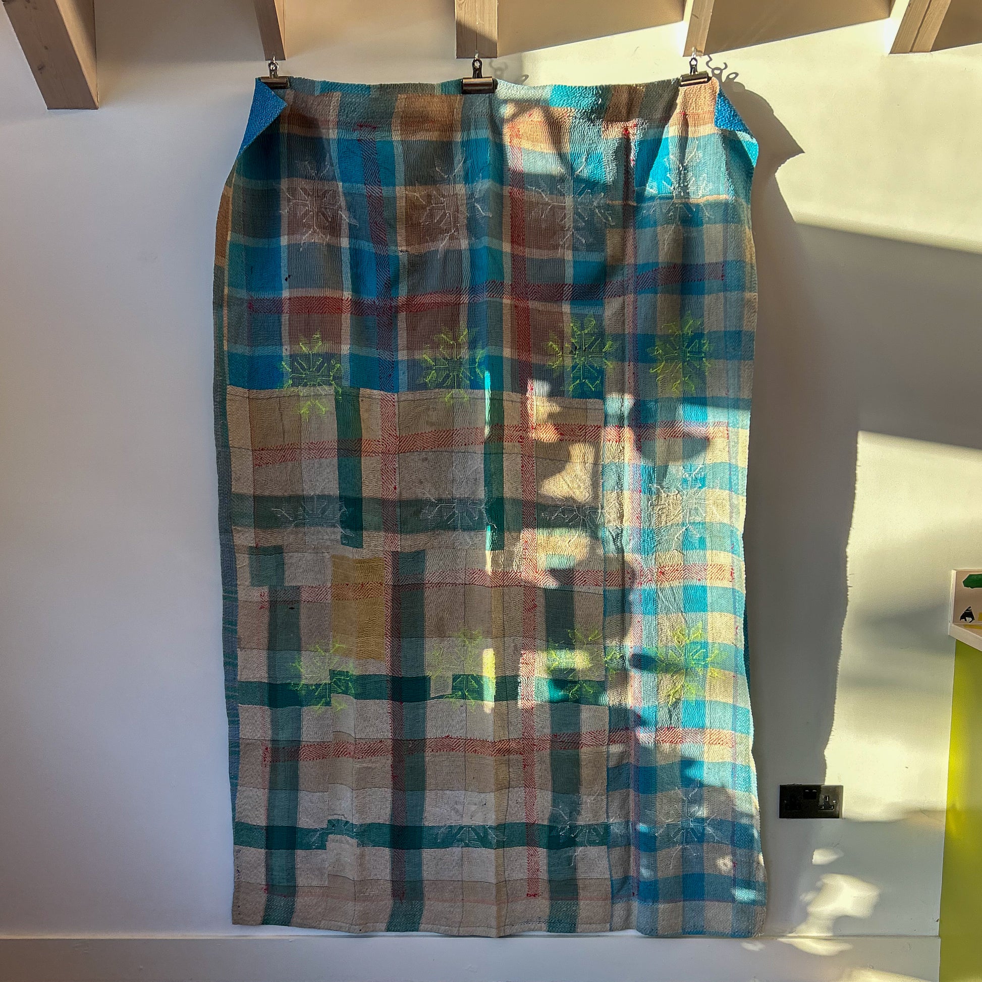 Plaid fabric hanging on a wooden rod against a white wall.