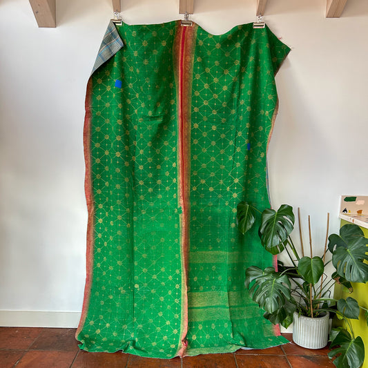 Green fabric with gold patterns draped over a wooden frame against a white wall with plants in the corner. kantha-vintage-2026 - hand-made-blanket-throw-textiles-wall-hanging