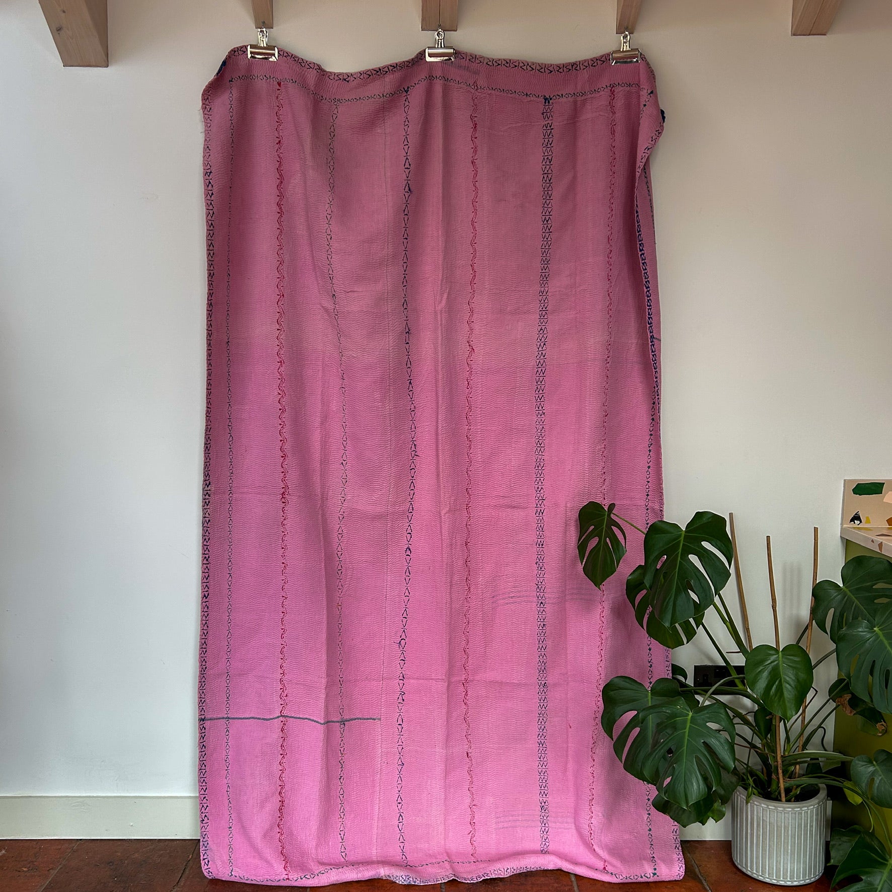 Pink curtain hanging on a wooden rod with a plant in the background. vintage kantha throw 2034 