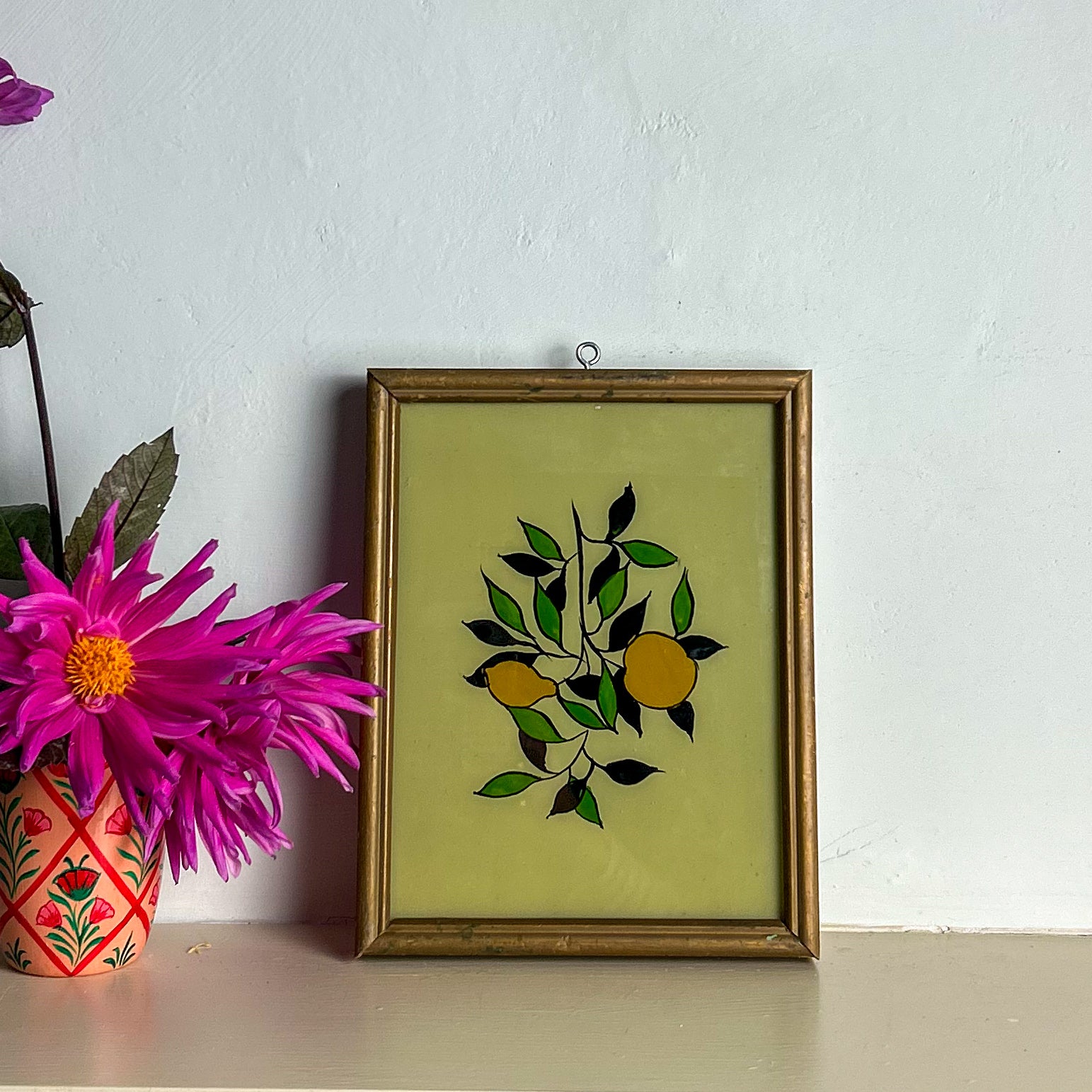 Framed artwork with lemons design on a white wall with a pink flower in the foreground.