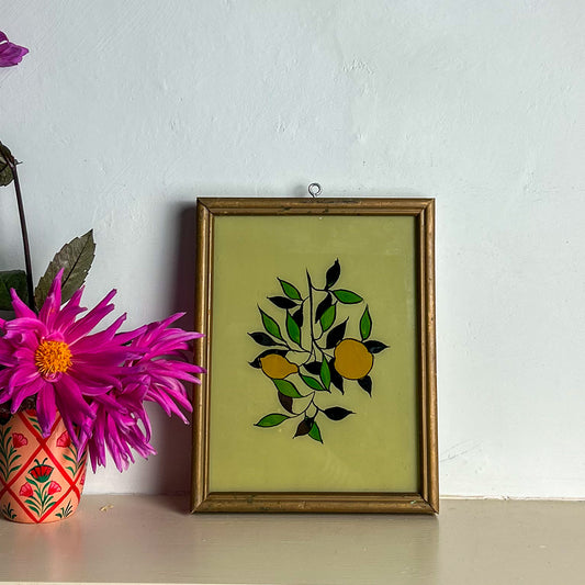 Framed artwork with lemons design on a white wall with a pink flower in the foreground.