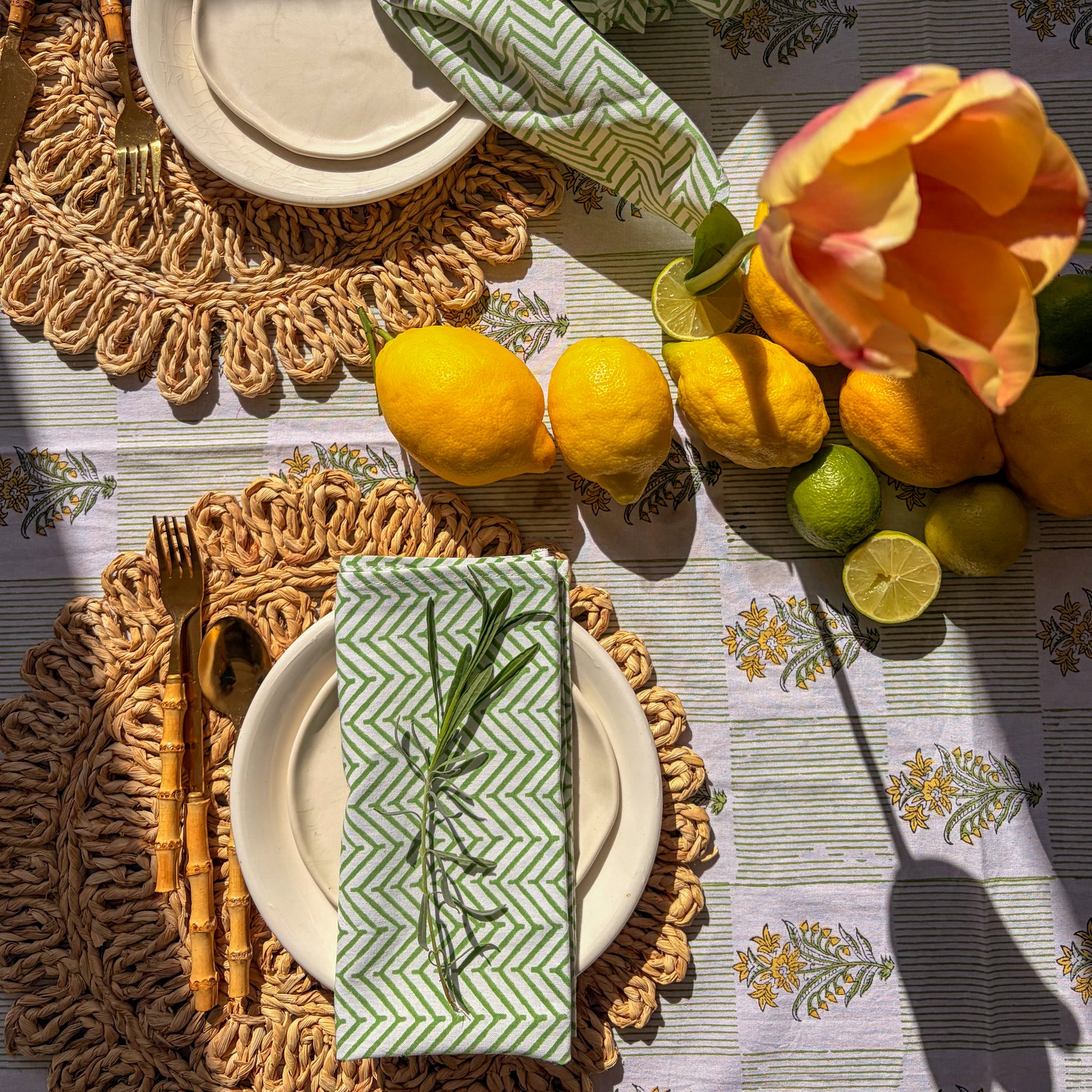 Table setting with lemons, limes, and a tulip on a patterned tablecloth.