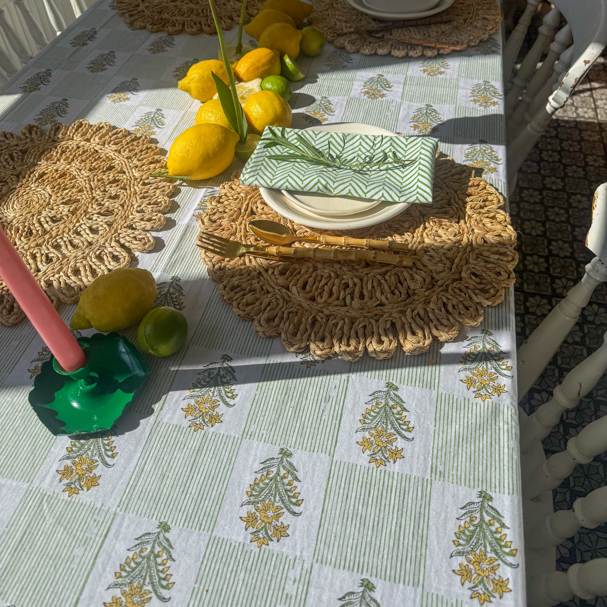 Table setting with lemons, green napkin, and decorative candles on a patterned tablecloth.