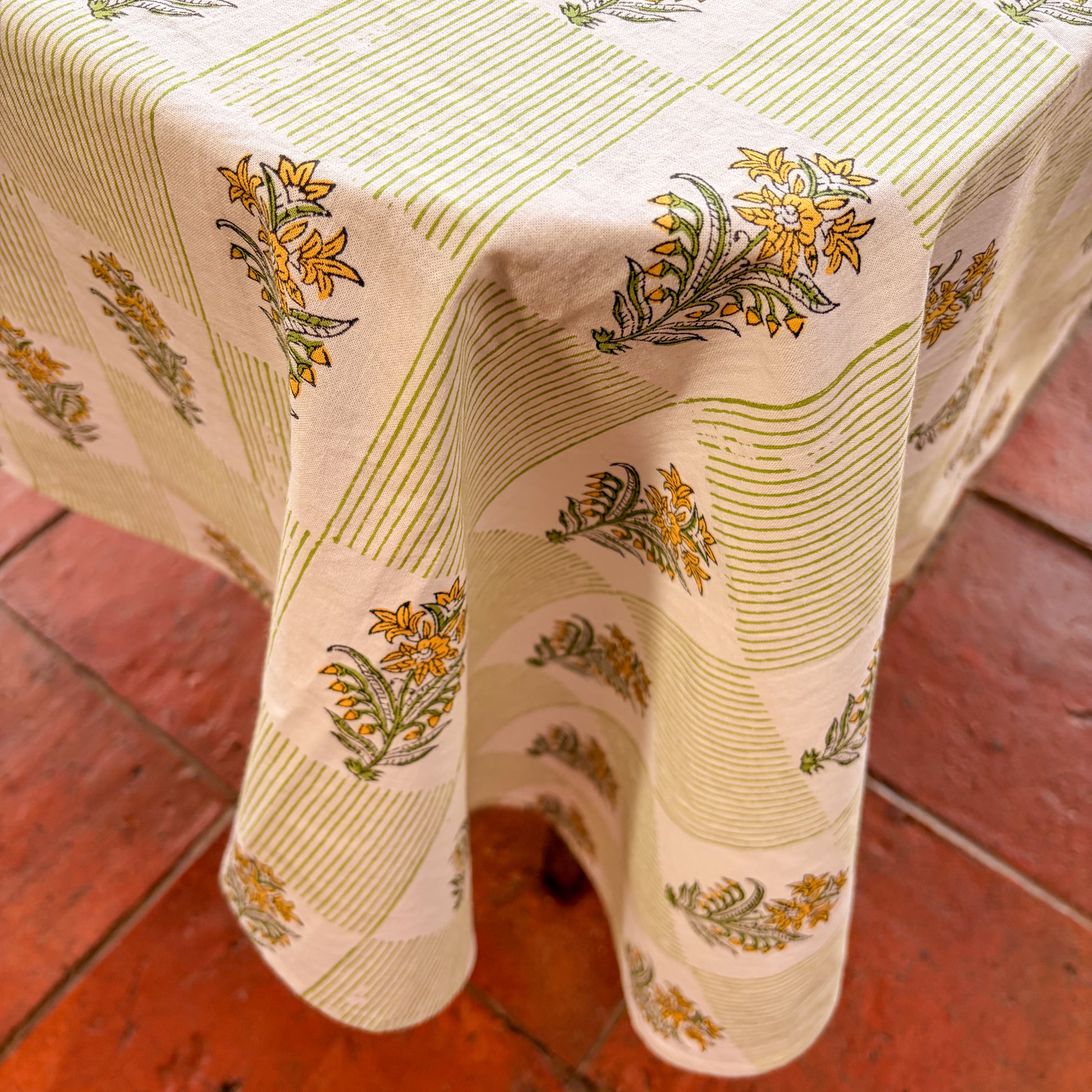 Floral-patterned tablecloth on a wooden table with a red brick floor background