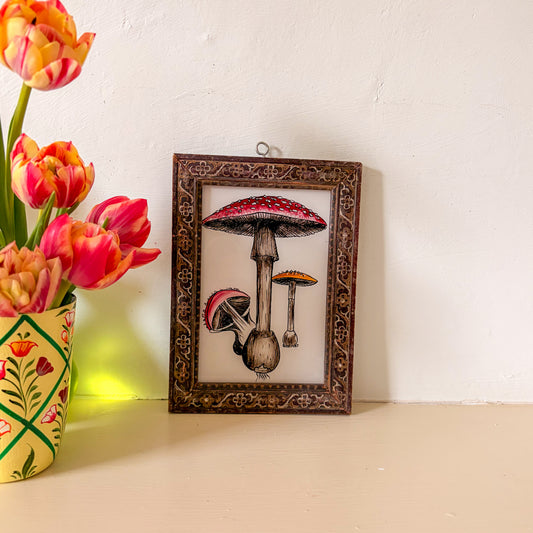Framed artwork of mushrooms on a shelf with tulips