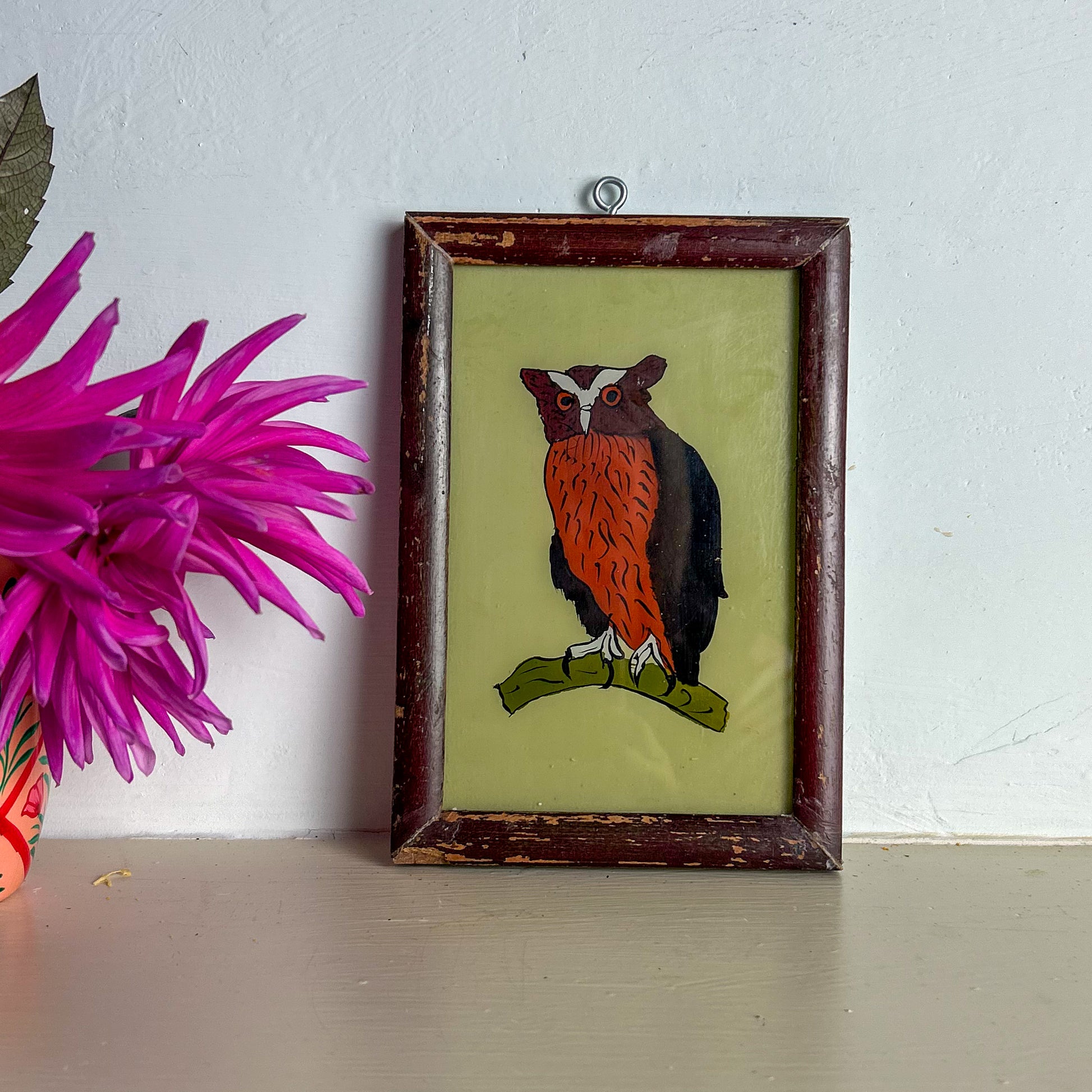 Framed artwork of an owl on a white wall with a pink flower in the foreground.