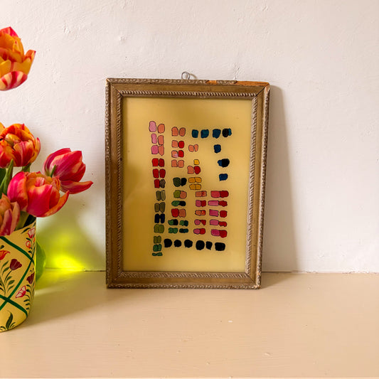 Framed artwork with colorful pattern next to a vase of tulips on a light surface.