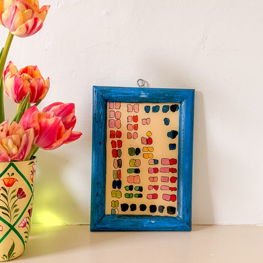 Framed artwork with colorful abstract design next to a vase with tulips on a white surface.