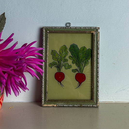 Framed artwork of radishes on a light blue wall with a pink flower.