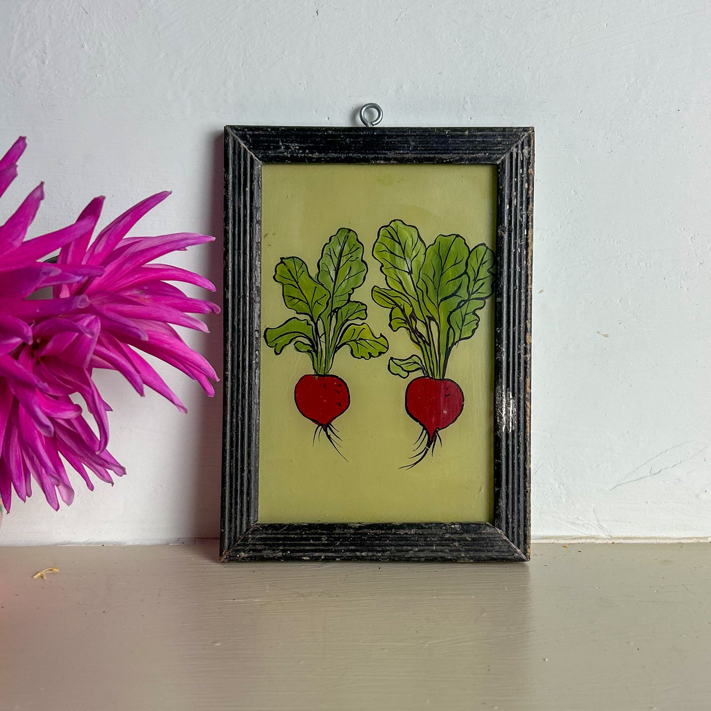 Framed artwork of two red radishes with green leaves on a light surface.