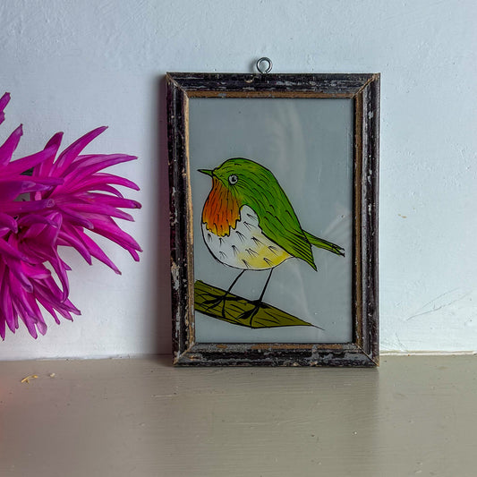 Framed illustration of a colorful bird next to a pink flower on a light blue wall.
