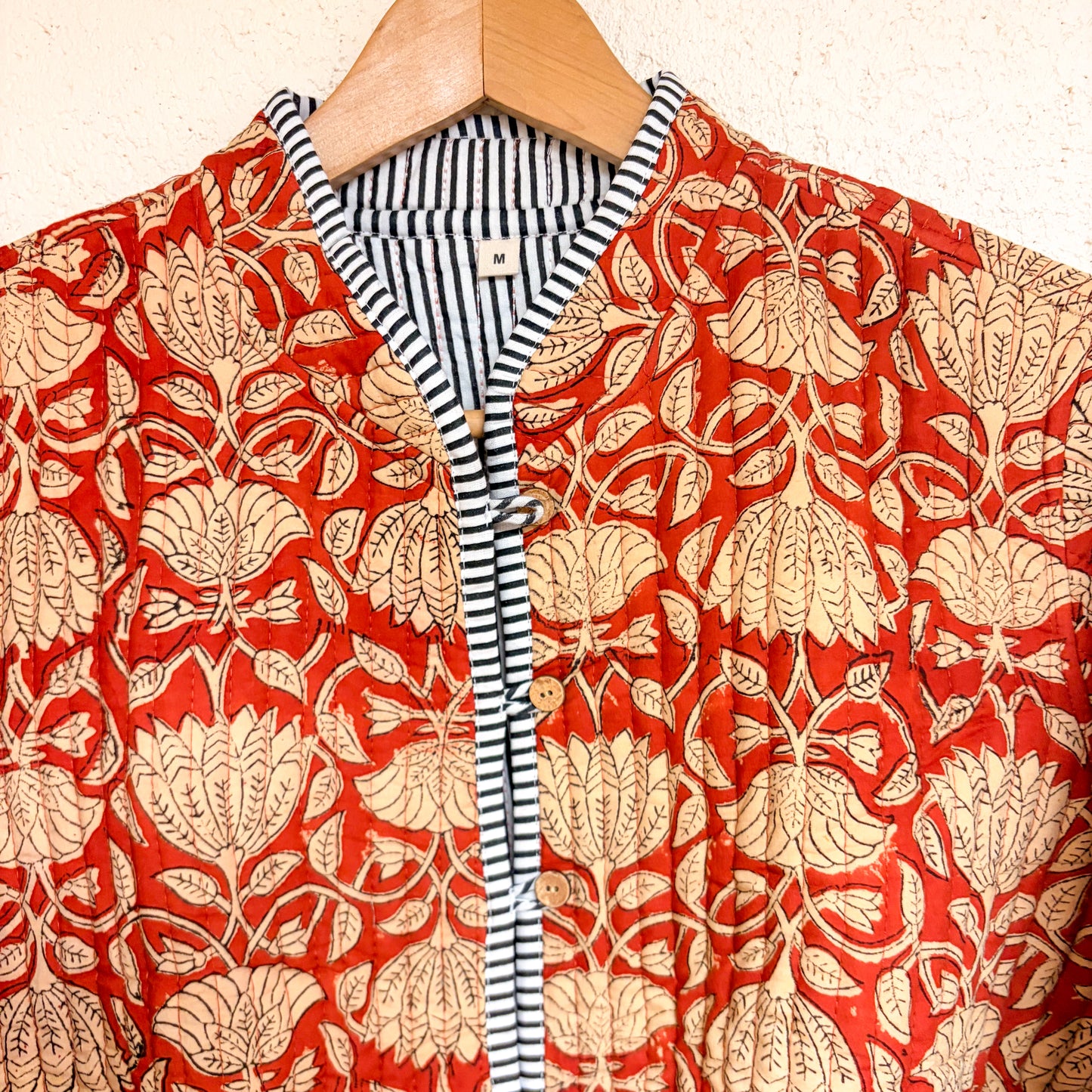 Red floral patterned garment on a hanger with a striped shirt underneath.