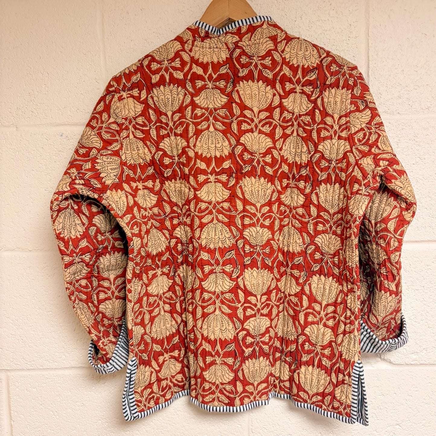 Red and beige patterned shirt on a wooden hanger against a white wall