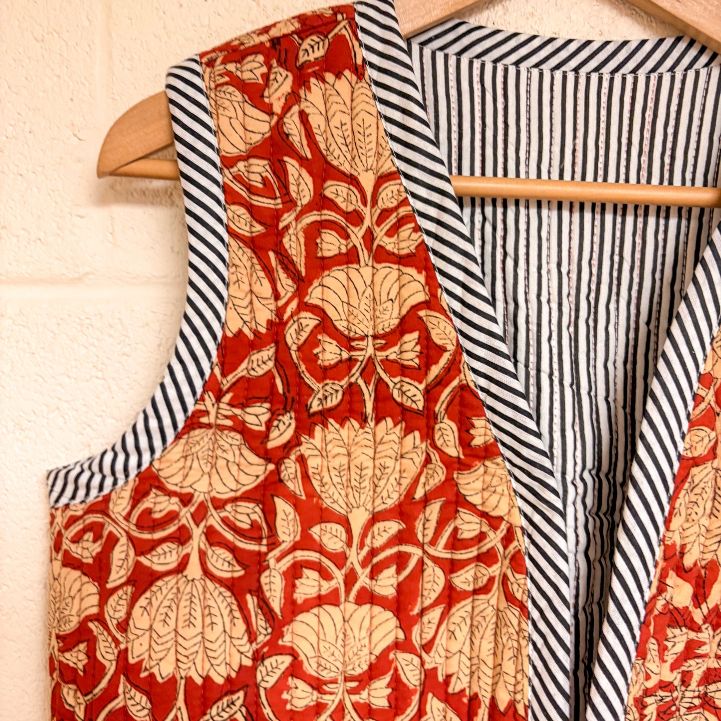 Red floral apron hanging on a wooden hanger with a striped fabric background.