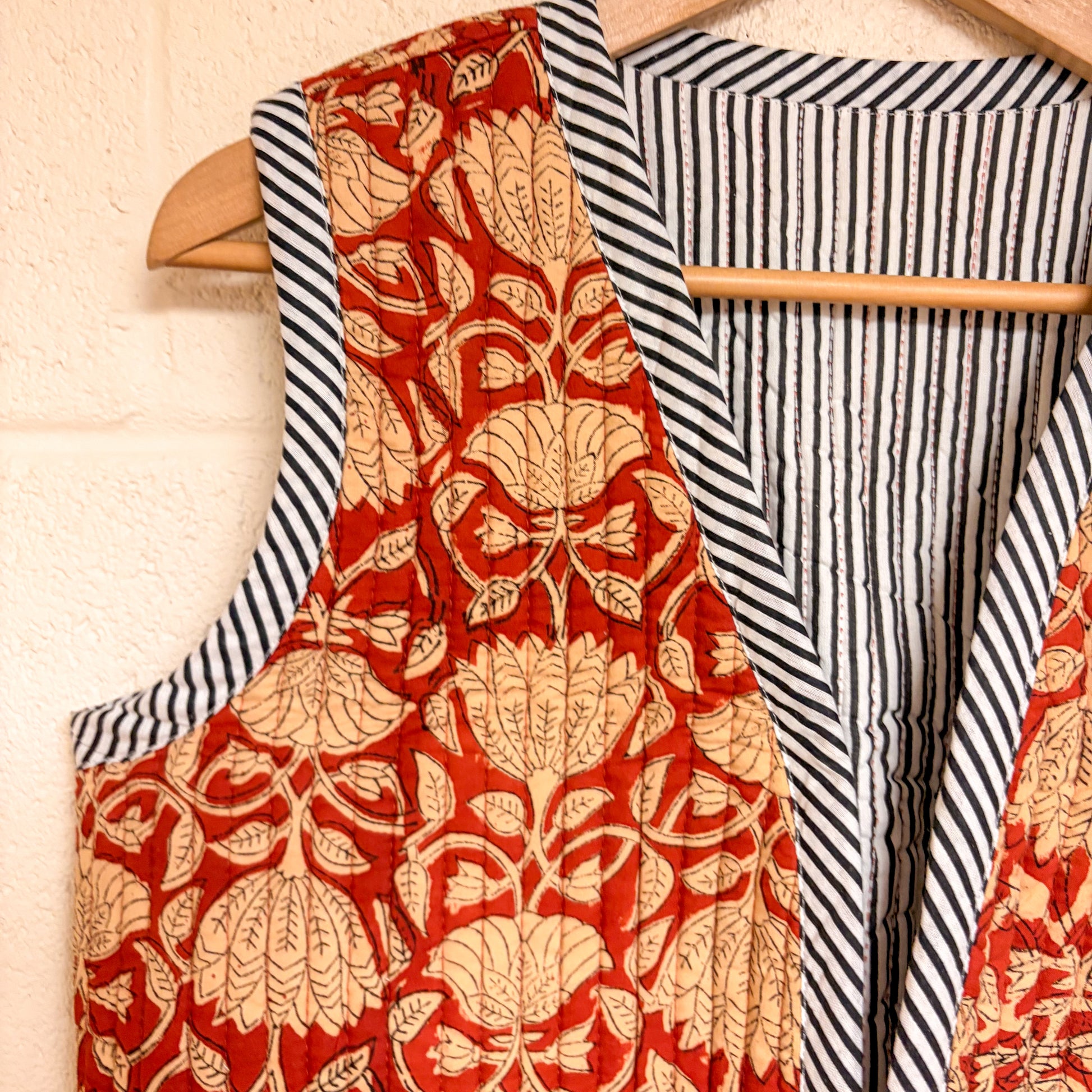 Red floral apron hanging on a wooden hanger with a striped fabric background.