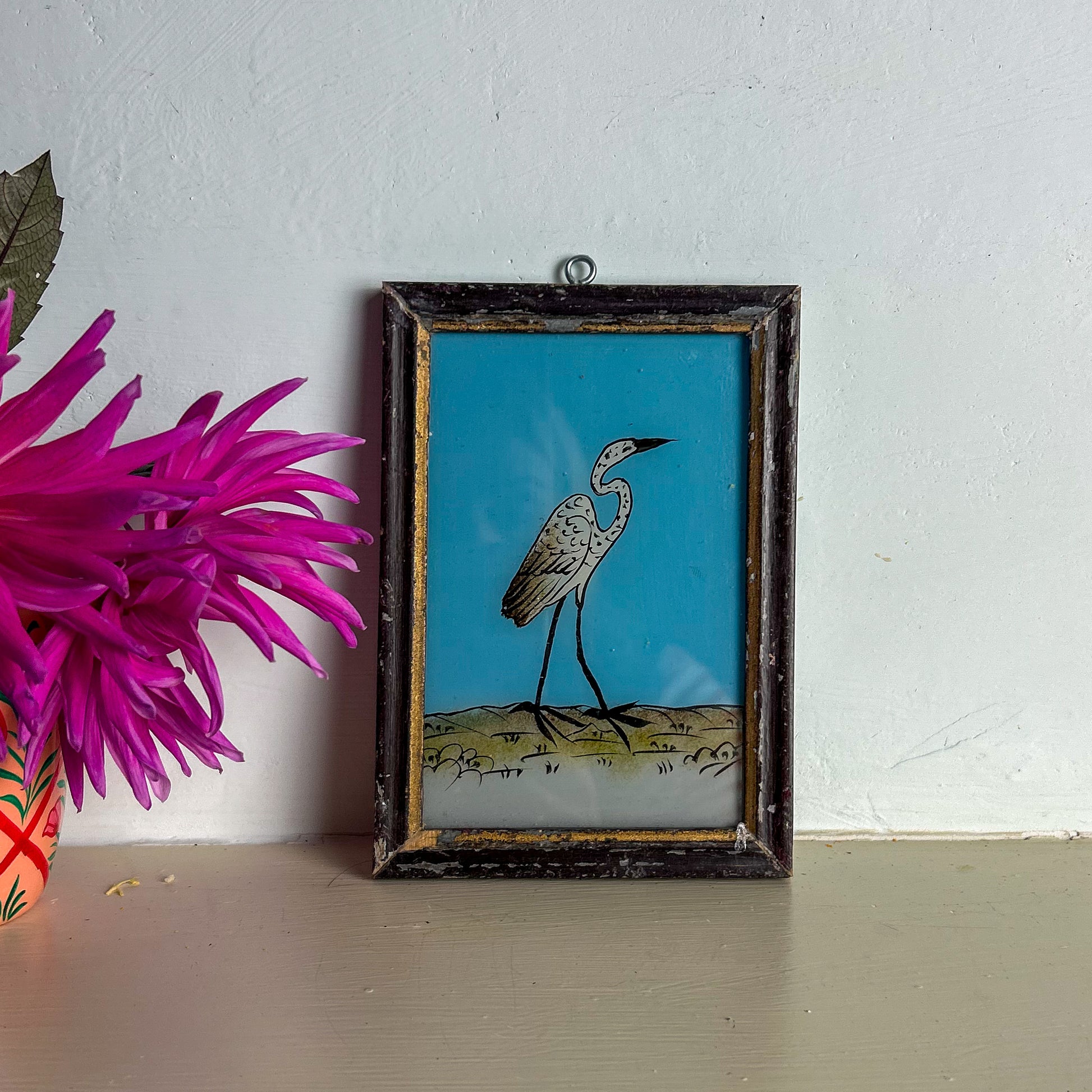 Framed artwork of a bird on a blue background next to a pink flower