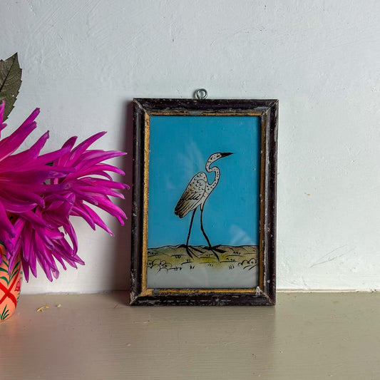 Framed artwork of a bird on a blue background next to a pink flower