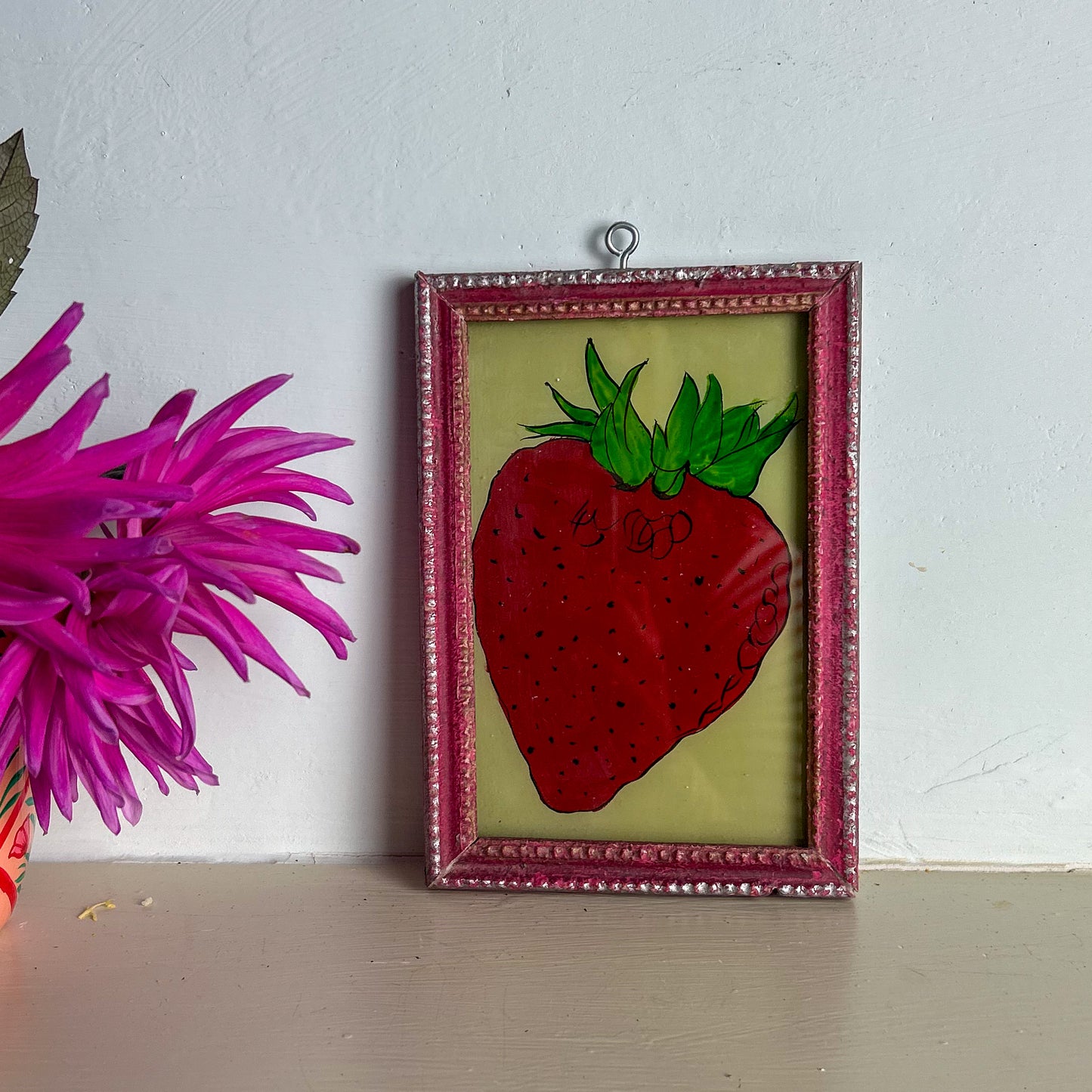 Framed artwork of a strawberry on a white wall with a pink flower.